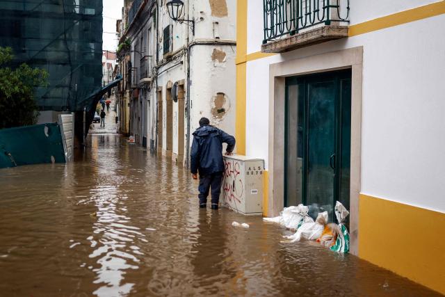 A man walks past a doorway protected by sandbags as floodwaters cover the street in Alcacer do Sal, south of Portugal, amid Storm Leonardo on February 4, 2026. A storm unleashing up to 35 centimetres (14 inches) of rain in 24 hours battered the Iberian Peninsula today, forcing thousands of people in southern Spain from their homes, shutting schools and cancelling trains. Leonardo compounded difficulties for residents in Portugal who were already reeling from last week's Storm Kristin, which killed five people, injured hundreds and cut off tens of thousands of customers from the power grid. (Photo by PATRICIA DE MELO MOREIRA / AFP)