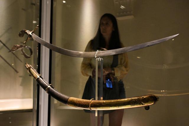 A woman looks at the curved saber that belonged to Argentine national hero General Jose de San Martin at the National Historical Museum in Buenos Aires on February 4, 2026. The decision by Javier Milei's government to move the saber of Argentine Liberator Jose de San Martin to a military regiment sparked indignation among the heirs of the piece, who demanded in court that the weapon remain in the National Historical Museum, where it was donated in 1897. (Photo by Luis ROBAYO / AFP)