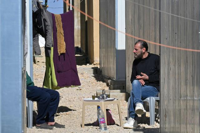 Two men sit together for hot drinks in an alley between shelters at the Imam Ali Housing Compound, where displaced Lebanese and Syrian refugee Shiite Muslims take refuge by the city of Hermel in Lebanon's northeastern Bekaa valley on February 4, 2026. (Photo by Joseph EID / AFP)