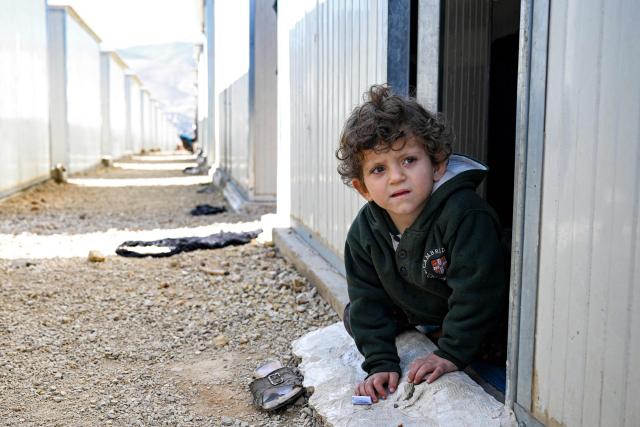 A boy sits at the entrance of one of the shelters at the Imam Ali Housing Compound, where displaced Lebanese and Syrian refugee Shiite Muslims take refuge by the city of Hermel in Lebanon's northeastern Bekaa valley on February 4, 2026. (Photo by Joseph EID / AFP)