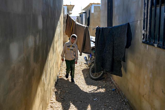 A boy walks past laundry drying on a line along an alley between shelters at the Imam Ali Housing Compound, where displaced Lebanese and Syrian refugee Shiite Muslims take refuge by the city of Hermel in Lebanon's northeastern Bekaa valley on February 4, 2026. (Photo by Joseph EID / AFP)