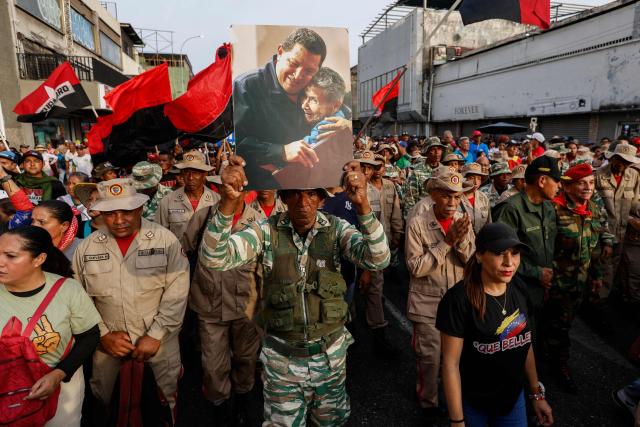 TOPSHOT - A member of the Bolivarian National Militia shows a portrait of late Venezuelan President Hugo Chavez during a march by 'Chavismo' supporters to commemorate the 34th anniversary of a coup attempt by Hugo Chavez, in Maracay, Aragua state, Venezuela, on February 4, 2026. (Photo by Pedro MATTEY / AFP)
