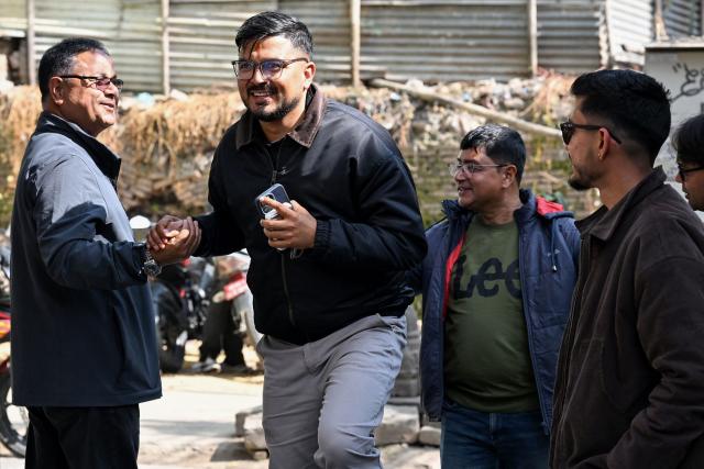 This photograph taken on February 3, 2026 shows Nepali Congress party election candidate Sachin Timalsena (2L) greeting a local (L) as he walks along a street in Kathmandu. Young election candidates are hoping to ride the wave of anger that toppled the previous government in Nepal, with 30 percent of the total registered for direct election aged under 40. The Himalayan country heads into landmark elections on March 5 -- the first since the deadly youth-led anti-corruption protest in 2025 spearheaded by protesters under the loose "Gen Z" umbrella title. (Photo by Prakash MATHEMA / AFP)