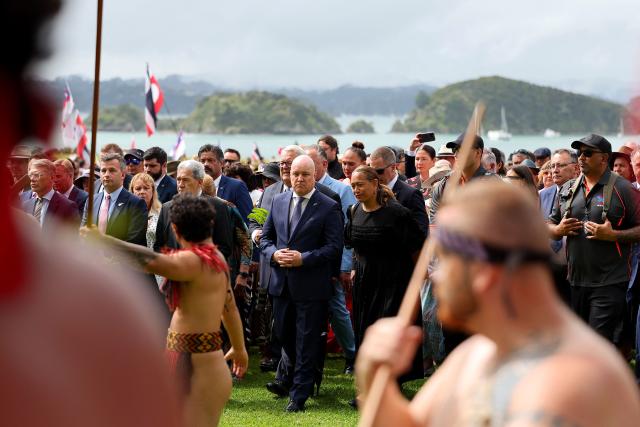 New Zealand Prime Minister Christopher Luxon (C), accompanied by fellow parliamentarians, attends a ceremony commemorating Waitangi Day in Waitangi on February 5, 2026. New Zealand's Prime Minister Christopher Luxon was heckled by a Maori crowd on February 5 during a speech marking national Waitangi Day celebrations, an annual political gathering that gives Indigenous tribes a chance to air grievances. (Photo by Ben STRANG / AFP)