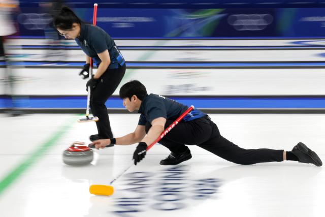 South Korea's Jeong Yeongseok curls the stone next to his teammate Kim Seonyeong in the curling mixed doubles round robin between South Korea and Italy during the Milano Cortina 2026 Winter Olympic Games at the Cortina Curling Olympic Stadium in Cortina d’Ampezzo on February 5, 2026. (Photo by Odd ANDERSEN / AFP)