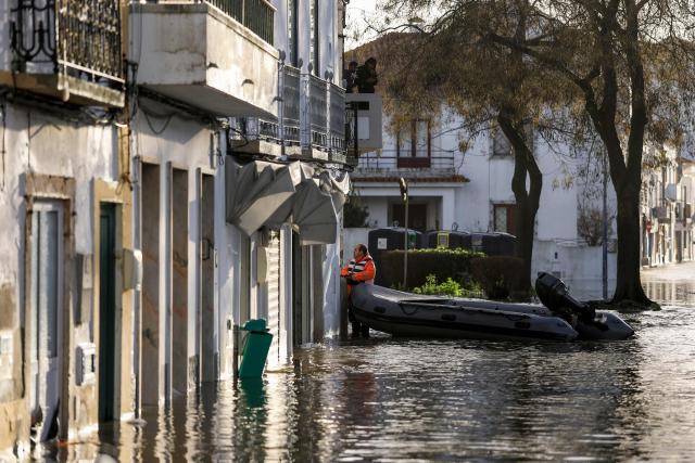A member of the Civil Protection holds an inflatable boat as he talks with residents while floodwaters cover the streets of Alcacer do Sal, south of Portugal, amid Storm Leonardo on February 5, 2026. Spain on February 5, 2026 lifted its highest weather alert for torrential rain in the southern region of Andalusia, where a woman went missing, a day after the storm killed one in Portugal. Storm Leonardo dumped more than 40 centimetres (15 inches) of rain in some Andalusian districts on February 4, the equivalent of several months of precipitation, forcing the evacuation of thousands, paralysing rail and road transport and shutting schools. The downpours came after a storm killed five people, injured hundreds and left tens of thousands without power in neighbouring Portugal last week. (Photo by PATRICIA DE MELO MOREIRA / AFP)