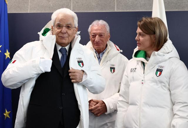 Italian President Sergio Mattarella (L) puts on an Italian delegation Olympic jacket as he visits the Olympic Village, as President of the Italian National Olympic Committee (CONI) Luciano Buonfiglio (C) reacts, ahead of the Milano Cortina 2026 Winter Olympic Games in Milan, on February 5, 2026. (Photo by Yara Nardi / POOL / AFP)