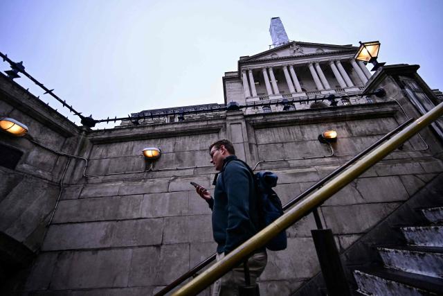 A man walks down into the understand station outside the Bank of England (back R) in central London on February 5, 2026. The Bank of England on February 5 cut its forecasts for UK growth this year and next, as it left its benchmark interest rate at 3.75 percent. (Photo by Ben STANSALL / AFP)