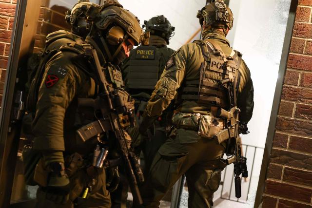 Federal agents with Homeland Security Investigations (HSI) enter a residential building seeking to detain a protestor in Minneapolis, Minnesota, on February 5, 2026. US President Donald Trump suggested on February 4 that a "softer touch" may be needed on immigration, as his administration said 700 federal officers would be pulled from Minnesota but that mass deportations would not stop. The fatal shootings of two protesters by federal officers in Minneapolis last month sparked widespread outrage in the United States and calls for an end to immigration raids in the Midwestern city, but Trump's administration has been reluctant to shift course. (Photo by CHARLY TRIBALLEAU / AFP)