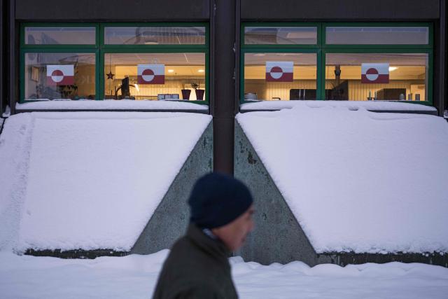 (FILES) A man walks past a building with Greenland flags hanging in the windows in downtown Nuuk, Greenland, on January 19, 2026. Canada and France, which both adamantly oppose Donald Trump's wish to control Greenland, will open consulates in the Danish autonomous territory's capital on February 6, 2026, a strong show of support for the local government. (Photo by Jonathan NACKSTRAND / AFP)