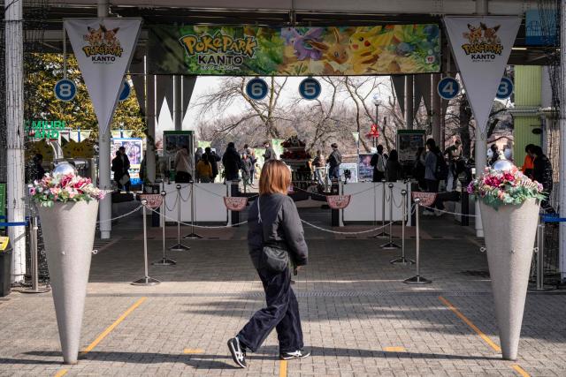 A woman walks past the gate of 'PokePark Kanto' in Inagi, Tokyo prefecture on February 6, 2026. The first permanent Pokemon theme park opened in Tokyo on February 5, featuring cute rides and a woodland area where visitors can try and "catch 'em all". (Photo by Yuichi YAMAZAKI / AFP)