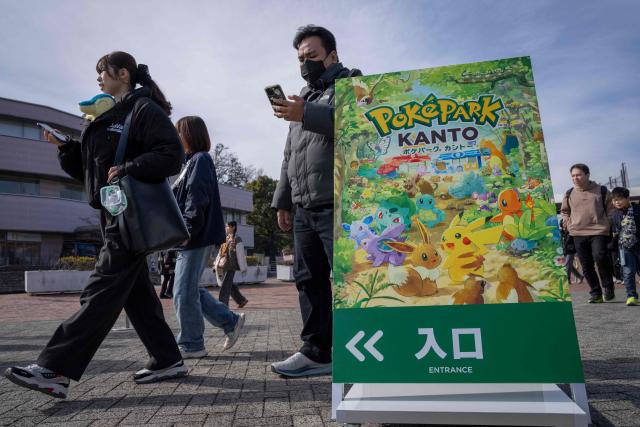 People walk past signage of 'PokePark Kanto' outside the Yomiuri Land amusement park in Inagi, Tokyo prefecture on February 6, 2026. The first permanent Pokemon theme park opened in Tokyo on February 5, featuring cute rides and a woodland area where visitors can try and "catch 'em all". (Photo by Yuichi YAMAZAKI / AFP)
