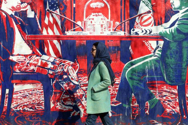 An Iranian woman walk past anti-US mural depicting Iran and US negotiation table, painted on the outer walls of the former US embassy, in Tehran on February 6, 2026. Iran's foreign minister met with his Omani counterpart in Muscat on February 6, ahead of Oman-mediated talks with the United States on the Islamic republic's nuclear programme. (Photo by AFP)