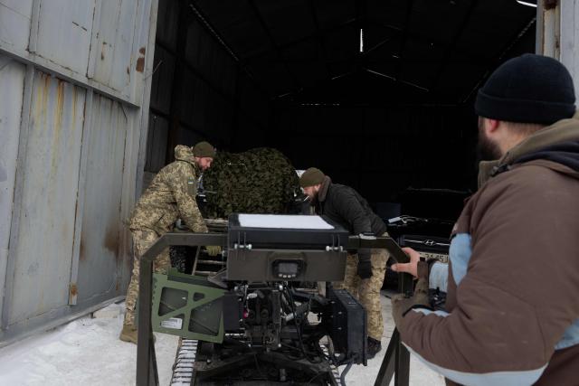 Ukrainian servicemen of the 30th separate mechanized brigade push a robotic combat vehicle armed with an Mk 19 grenade launcher to load it onto a military vehicle after testing it at an undisclosed location in Donetsk region on January 27, 2026, amid the Russian invasion of Ukraine. (Photo by Tetiana DZHAFAROVA / AFP)