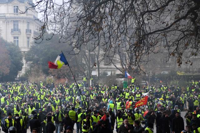 (FILES) Demonstrators gather as a French flag floats during a protest of Yellow vests (Gilets jaunes) against rising oil prices and living costs, on December 1, 2018 in Paris. Nine CRS police officers will appear before the Paris courthouse on February 9, 2026 for violence committed against Yellow Vests in a Burger King in 2018. (Photo by Alain JOCARD / AFP)