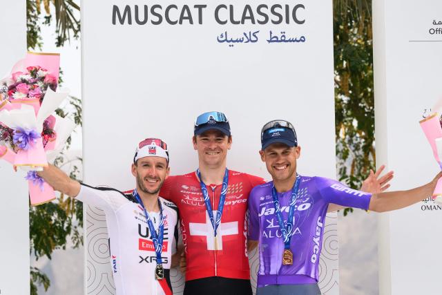 Team Jayco AlUla Swiss rider Mauro Schmid (C) celebrates on the podium after winning the Muscat Classic cycling race, flanked by second placed UAE Team Emirates XRG British rider Adam Yates (L) and third placed Team Jayco AlUla Australian rider Lucas Plapp in Muscat, on February 6, 2026. (Photo by Loic VENANCE / AFP)
