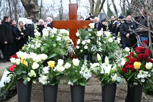 Flowers and a cross are seen at the grave of Hungarian filmmaker Bela Tarr as people attend his funeral at the Fiumei Road Cemetery of Budapest, Hungary, on February 6, 2026, one month after his death. Legendary Hungarian filmmaker Bela Tarr, known for his long takes, monochromatic movies and depictions of desolate landscapes on the silver screen, died on January 6, 2026 at the age of 70. Tarr was best known for the movie "Satantango (1994), a seven-hour epic about the collapse of communism in Eastern Europe and its material and spiritual decline. (Photo by Attila KISBENEDEK / AFP)