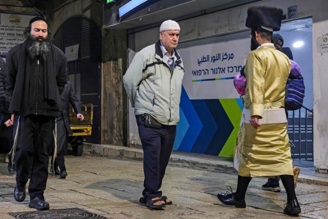 A Palestinian man (C) walks past ultra-Orthodox Jews in the old city of Jerusalem on February 6, 2026 (Photo by AHMAD GHARABLI / AFP)