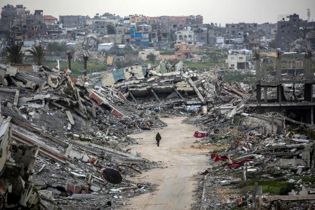 TOPSHOT - A man walks along a street past the rubble of destroyed buildings in the Zahra neighbourhood, southwest of Nuseirat in the central Gaza Strip, on February 6, 2026. Since October 10, a fragile US-sponsored truce in Gaza has largely halted the fighting between Israeli forces and Hamas, but both sides have alleged frequent violations. (Photo by Eyad Baba / AFP)
