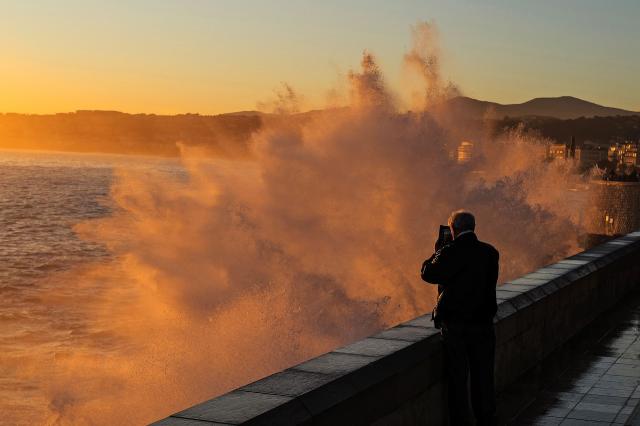 A man takes photographs of big waves at sunset on the French riviera city of Nice, on February 6, 2026. (Photo by Valery HACHE / AFP)