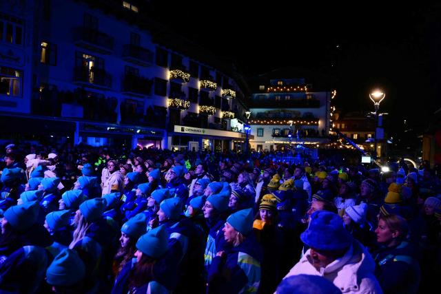 Volunteers and athletes react as they watch the speech of the President of the Organising Committee for the 2026 Olympic and Paralympic Winter Games during the opening ceremony of the Milano Cortina 2026 Winter Olympic Games Piazza Angelo Dibona in Cortina d'Ampezzo, northern Italy, on February 6, 2026. (Photo by Stefano RELLANDINI / POOL / AFP)