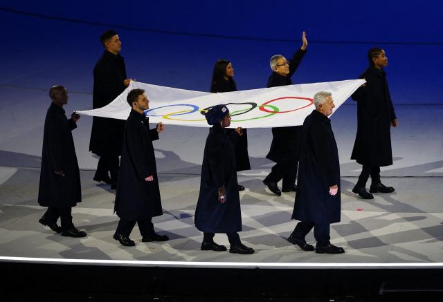 The Olympic Flag is carried by Tadatoshi Akiba, Rebeca Andrade, Maryam Bukar Hassan, Nicolo Govoni, Filippo Grandi, Eliud Kipchoge, Cindy Ngamba, Pita Taufatofua, figures committed to promoting peace, rights, and solidarity, during the opening ceremony of the Milano Cortina 2026 Winter Olympic Games at the San Siro stadium in Milan, northern Italy, on February 6, 2026. (Photo by Susana Vera / POOL / AFP)