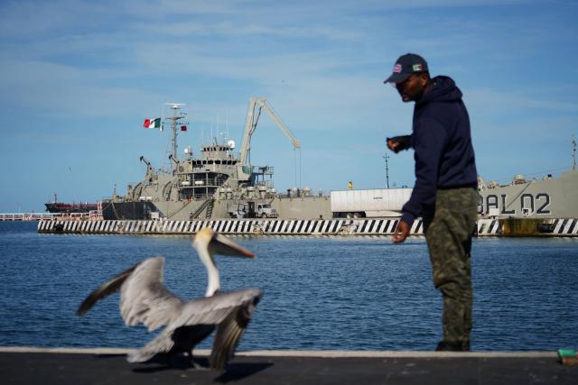 TOPSHOT - A man feeds a pelican with the Isla Holbox (BAL-02) vessel belonging to the Mexican Navy (SEMAR) in the background, intended for humanitarian aid, which is docked at Veracruz port in Veracruz, Mexico, on February 6, 2026. Mexico will ship humanitarian aid to Cuba in the coming days while continuing to negotiate with Washington on the possibility of circumventing a US oil siege, President Claudia Sheinbaum said on February 6. (Photo by Victoria Razo / AFP)