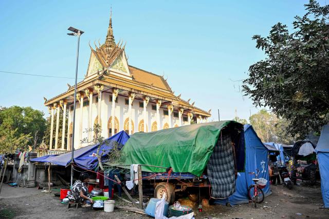 A woman, displaced after clashes between Thai and Cambodian soldiers, washes plates and bowls in front of her shelter in an evacuation centre on the grounds of a pagoda in Banteay Meanchey province on February 4, 2026. A sign hanging from a rusty ice-green shipping container installed by Thai forces on what they say is the border with Cambodia proclaims: "Cambodian citizens are strictly prohibited from entering this area." (Photo by TANG CHHIN Sothy / AFP) / To go with 'THAILAND-CAMBODIA-CONFLICT-BORDER,REPORTAGE' by Suy SE and Montira RUNGJIRAJITTRANON