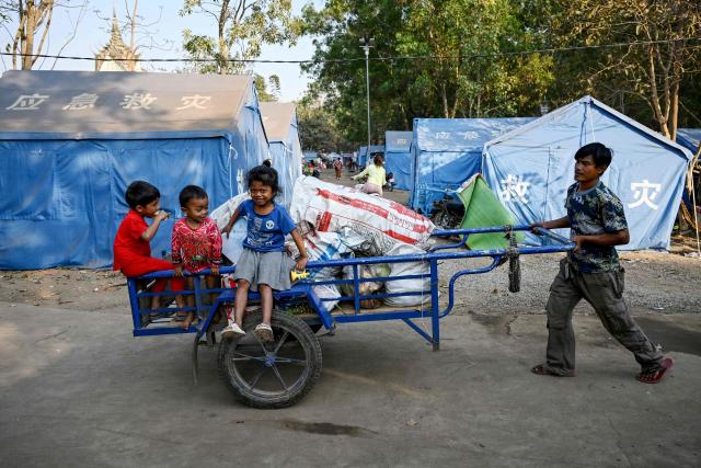 A man, displaced after clashes between Thai and Cambodian soldiers, pushes a cart loaded with his belongings as children ride in it through an evacuation centre on the grounds of a pagoda in Banteay Meanchey province on February 4, 2026. A sign hanging from a rusty ice-green shipping container installed by Thai forces on what they say is the border with Cambodia proclaims: "Cambodian citizens are strictly prohibited from entering this area." (Photo by TANG CHHIN Sothy / AFP) / To go with 'THAILAND-CAMBODIA-CONFLICT-BORDER,REPORTAGE' by Suy SE and Montira RUNGJIRAJITTRANON
