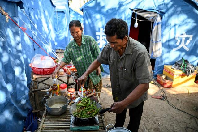 Farmer Sok Chork, displaced after clashes between Thai and Cambodian soldiers, cooks a meal in front of his tent in an evacuation centre on the grounds of a pagoda in Banteay Meanchey province on February 4, 2026. A sign hanging from a rusty ice-green shipping container installed by Thai forces on what they say is the border with Cambodia proclaims: "Cambodian citizens are strictly prohibited from entering this area." (Photo by TANG CHHIN Sothy / AFP) / To go with 'THAILAND-CAMBODIA-CONFLICT-BORDER,REPORTAGE' by Suy SE and Montira RUNGJIRAJITTRANON