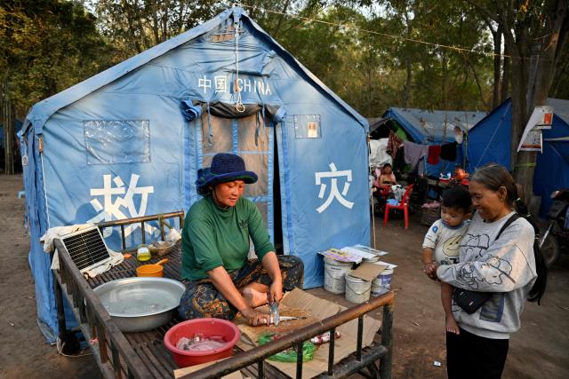 A woman, displaced after clashes between Thai and Cambodian soldiers, prepares fish in front of her tent in an evacuation centre on the grounds of a pagoda in Banteay Meanchey province on February 4, 2026. A sign hanging from a rusty ice-green shipping container installed by Thai forces on what they say is the border with Cambodia proclaims: "Cambodian citizens are strictly prohibited from entering this area." (Photo by TANG CHHIN Sothy / AFP) / To go with 'THAILAND-CAMBODIA-CONFLICT-BORDER,REPORTAGE' by Suy SE and Montira RUNGJIRAJITTRANON
