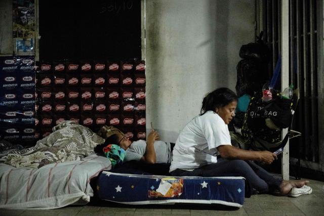 Two women watch their mobile phones as they camp outside El Rodeo I prison as they wait for news of prisoner releases in Guatire, Miranda state, some 30 kilometers east of Caracas, on February 6, 2026. Venezuela's parliament chief, a former member of ousted leader Nicolas Maduro's inner circle, on February 6 promised the speedy release of remaining political prisoners during a meeting with their relatives. "By Friday (February 13) at the latest they will all be free," Jorge Rodriguez told prisoners' families outside the notorious Zona 7 detention center in Caracas. (Photo by Maryorin Mendez / AFP)