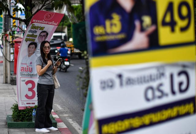A pedestrian waits on the sidewalk between campaign posters on the eve of Thailand's general election in Bangkok on February 7, 2026. (Photo by Amaury PAUL / AFP)