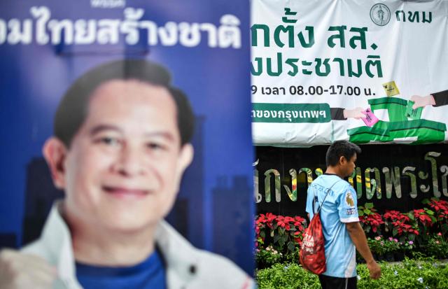 A pedestrian walks in front of an electoral information banner and past a campaign poster of United Thai Nation Party's prime ministerial candidate Pirapan Salirathavibhaga (L) on the eve of Thailand's general election in Bangkok on February 7, 2026. (Photo by Amaury PAUL / AFP)