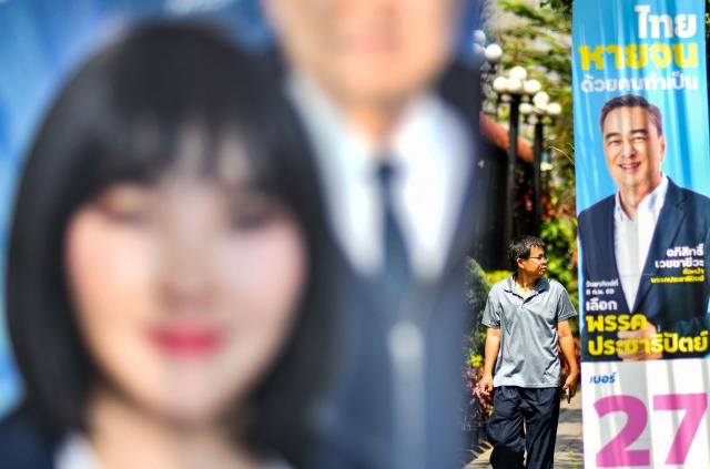 A pedestrian walks past a campaign poster of the Democrat Party's prime ministerial candidate Abhisit Vejjajiva (R) on the eve of Thailand's general election in Bangkok on February 7, 2026. (Photo by Amaury PAUL / AFP)