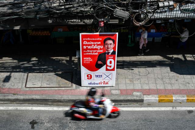 A motorist rides in front of a campaign poster of Pheu Thai Party's prime ministerial candidate Yodchanan Wongsawat on the eve of Thailand's general election in Bangkok on February 7, 2026. (Photo by Amaury PAUL / AFP)