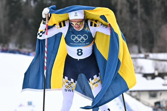 Sweden's Frida Karlsson holds Norway's national flag towards the finish on her way to win the women's cross country 10km + 10km skiathlon event of the Milano Cortina 2026 Winter Olympic Games at Tesero Cross-Country Skiing Stadium in Lago di Tesero (Val di Fiemme) on February 7, 2026. (Photo by Javier SORIANO / AFP)