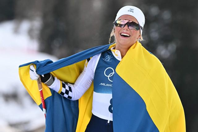 Sweden's Frida Karlsson holds Norway's national flag towards at the finish line aftet winning the women's cross country 10km + 10km skiathlon event of the Milano Cortina 2026 Winter Olympic Games at Tesero Cross-Country Skiing Stadium in Lago di Tesero (Val di Fiemme) on February 7, 2026. (Photo by Javier SORIANO / AFP)