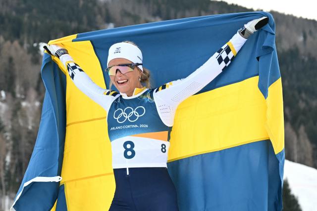 Sweden's Frida Karlsson holds Sweden's national flag  after winning the women's cross country 10km + 10km skiathlon event of the Milano Cortina 2026 Winter Olympic Games at Tesero Cross-Country Skiing Stadium in Lago di Tesero (Val di Fiemme) on February 7, 2026. (Photo by Javier SORIANO / AFP)