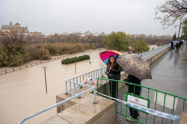 Pedestrians holding their umbrella observe the flooded bank of the Guadalquivir River in Cordoba on February 7, 2026. Spain and Portugal on February 7, 2026 braced for another storm heading for the Iberian peninsula, just days after the floods caused by Storm Leonardo killed at least one person in each country. (Photo by JORGE GUERRERO / AFP)