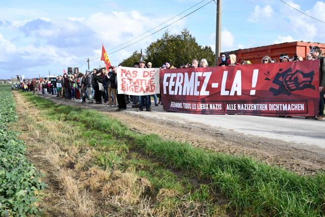 Members of the collective “Fermez la!” gather behind banners and placards as they take part in a demonstration for the closure of a hangar, "La Taverne de Thor", that has hosted MMA gatherings and neo-Nazi concerts for over ten years at Combres-sous-les-Cotes, north-eastern France on February 7, 2026. (Photo by Jean-Christophe VERHAEGEN / AFP)