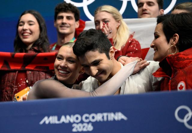 Canada's Marjorie Lajoie (L) and Canada's Zachary Lagha (C) hug in the kiss and cry area after competing in the figure skating team event ice dance-free dance during the Milano Cortina 2026 Winter Olympic Games at Milano Ice Skating Arena in Milan on February 7, 2026. (Photo by WANG Zhao / AFP)