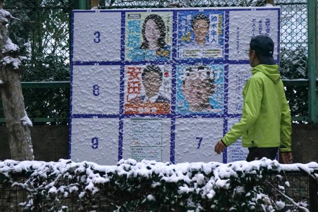 A man walks past a board displaying posters of candidates for the Lower House election, which is being held February 8, along the street amidst the falling snow in Tokyo, on February 8, 2026. (Photo by Kazuhiro NOGI / AFP)