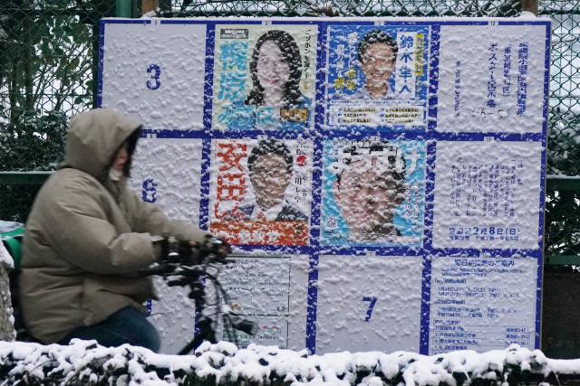 A person rides past a board displaying posters of candidates for the Lower House election, which is being held February 8, is seen along the street amidst the falling snow in Tokyo, on February 8, 2026. (Photo by Kazuhiro NOGI / AFP)