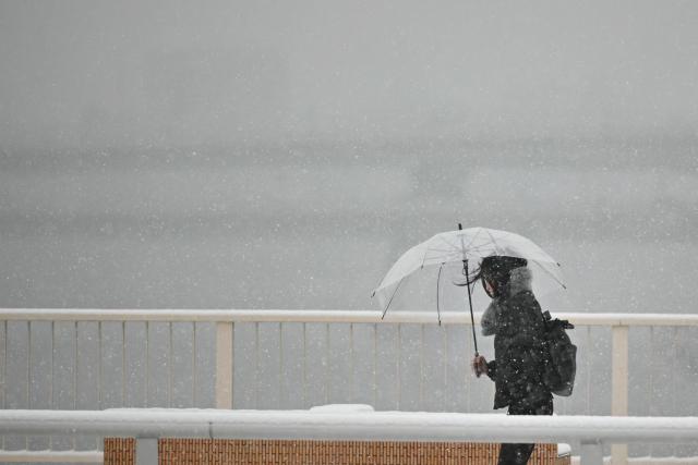 A pedestrian walks along the Shin-Ohashi bridge as snow falls in Tokyo on February 8, 2026. (Photo by Philip FONG / AFP)