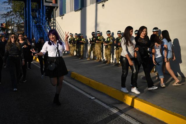 A fan of Colombian singer Shakira poses for a photo in front of members of the Salvadoran military outside the Jorge “Magico” Gonzalez National Stadium ahead of her first concert of the tour in El Salvador, in San Salvador on February 7, 2026. (Photo by Marvin RECINOS / AFP)