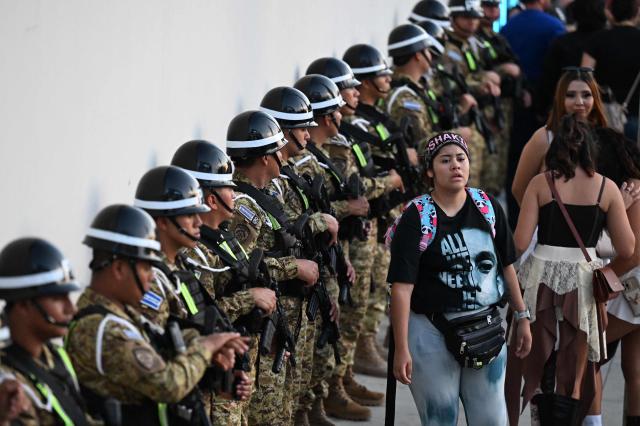 Fans of Colombian singer Shakira pass in front of members of the Salvadoran military outside the Jorge “Magico” Gonzalez National Stadium ahead of her first concert of the tour in El Salvador, in San Salvador on February 7, 2026. (Photo by Marvin RECINOS / AFP)