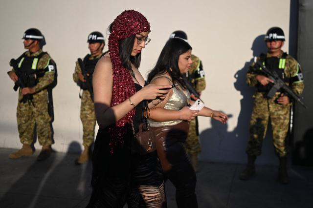 Fans of Colombian singer Shakira pass in front of members of the Salvadoran military outside the Jorge “Magico” Gonzalez National Stadium ahead of her first concert of the tour in El Salvador, in San Salvador on February 7, 2026. (Photo by Marvin RECINOS / AFP)