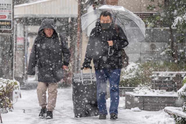 People walk through Nakano area during a snowfall in Tokyo on February 8, 2026. (Photo by Yuichi YAMAZAKI / AFP)