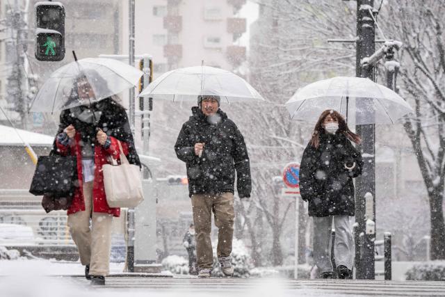 People cross a street during a snowfall in Tokyo on February 8, 2026. (Photo by Yuichi YAMAZAKI / AFP)